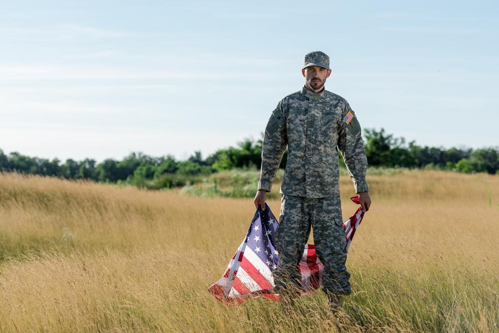 schöner Soldat in Tarnuniform mit amerikanischer Flagge im goldenen Feld  - Foto, Bild