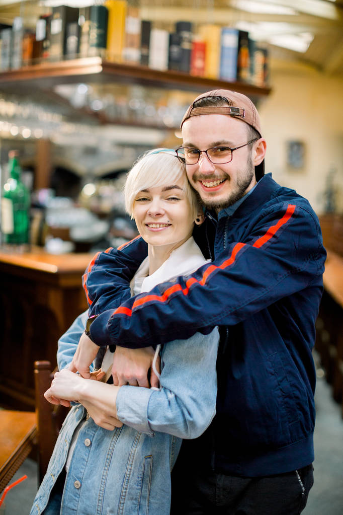 przystojny chłopak przytulanie uśmiechnięta dziewczyna podczas dnia w kawiarni. Uśmiechnięta kreatywna para przytulanie w kawiarni - Zdjęcie, obraz