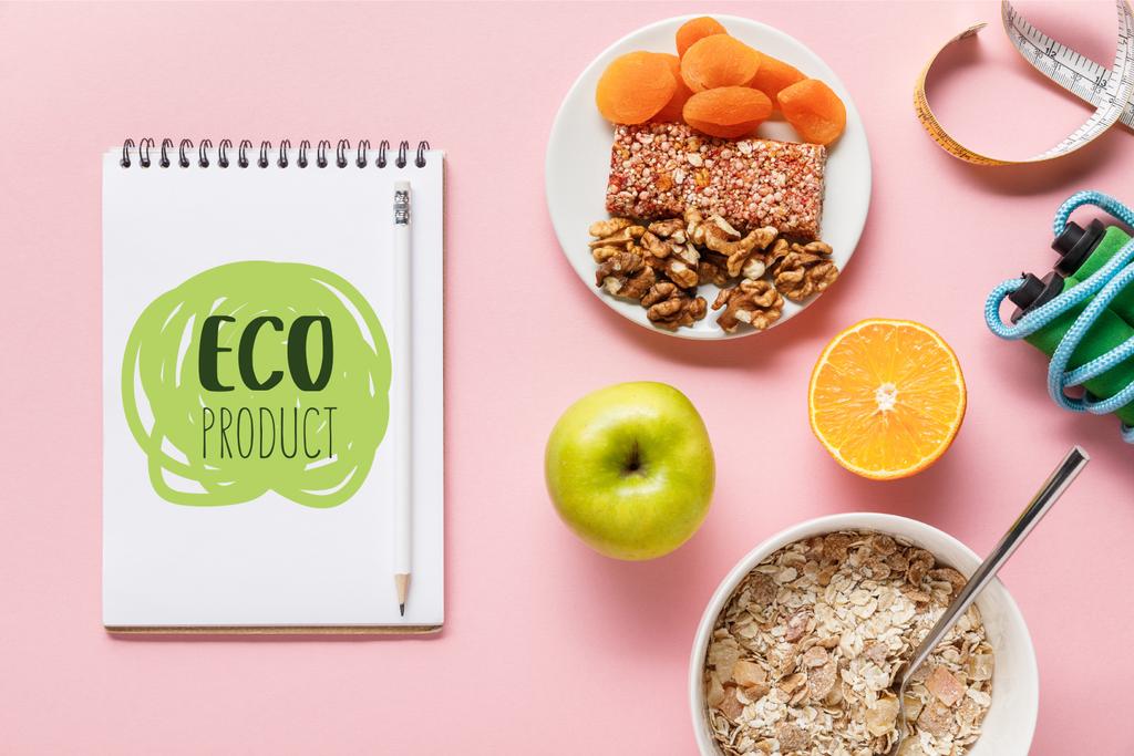 Widok z góry na świeże potrawy dietetyczne, taśmy pomiarowe, skakanie liny i notebooka z napisem eko produktu na różowym tle  - Zdjęcie, obraz