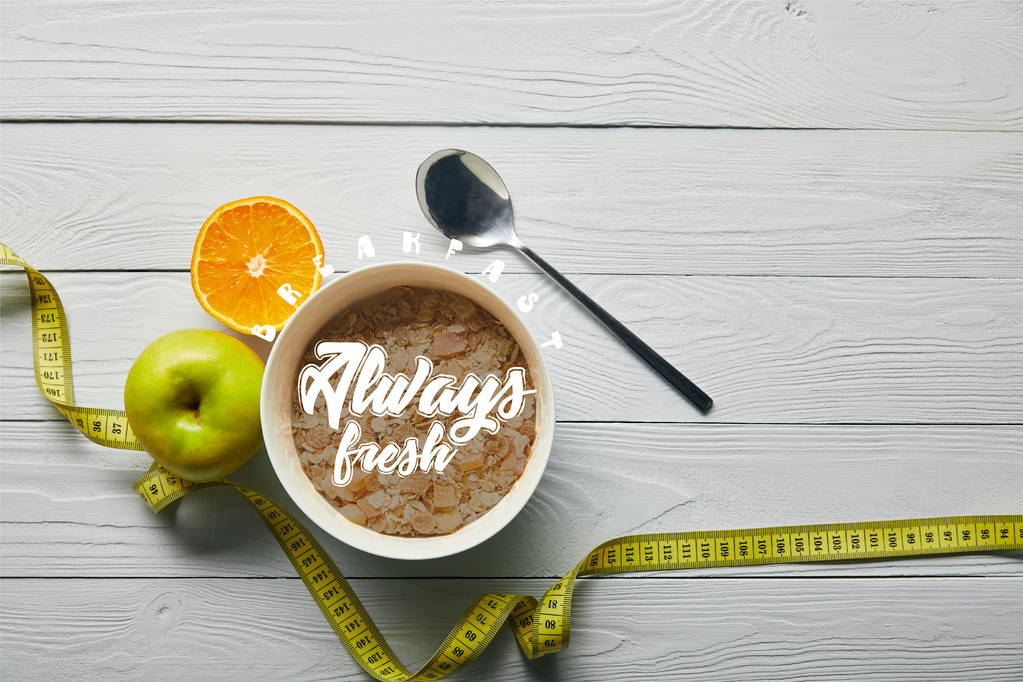 pohled na měřicí pásku, lžíci a snídani v misce blízko jablek a pomerančů na dřevěné bílé pozadí se snídaní vždy čerstvé písmo - Fotografie, Obrázek