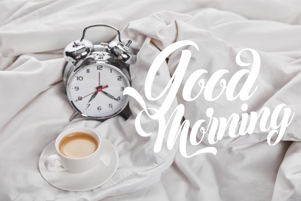 おはようイラスト付きベッドの銀目覚まし時計の近くにソーサーの白いカップでコーヒー ロイヤリティフリー写真 画像素材