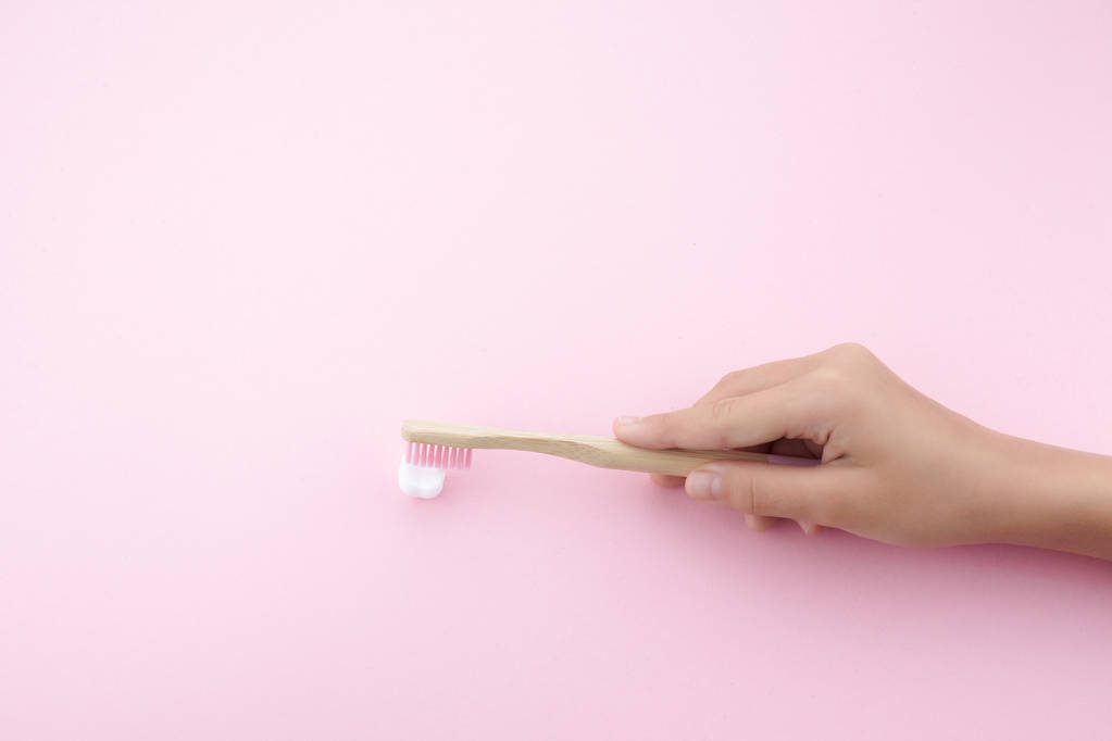 childs hand with toothbrush and white platic tooth on pink background - Photo, Image