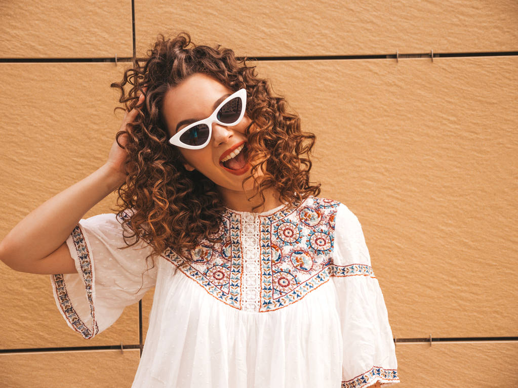 Gyönyörű mosolygó modell afro fürtök frizura öltözött nyári csípő fehér ruhában és napszemüveget. Szexi gondtalan lány pózol az utcán, közel sárga fal. Vicces és pozitív nő szórakoztunk - Fotó, kép