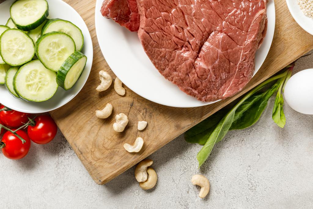 свіже сире м'ясо на білій тарілці біля горіхів та огірків, кетогенне меню дієти
 - Фото, зображення