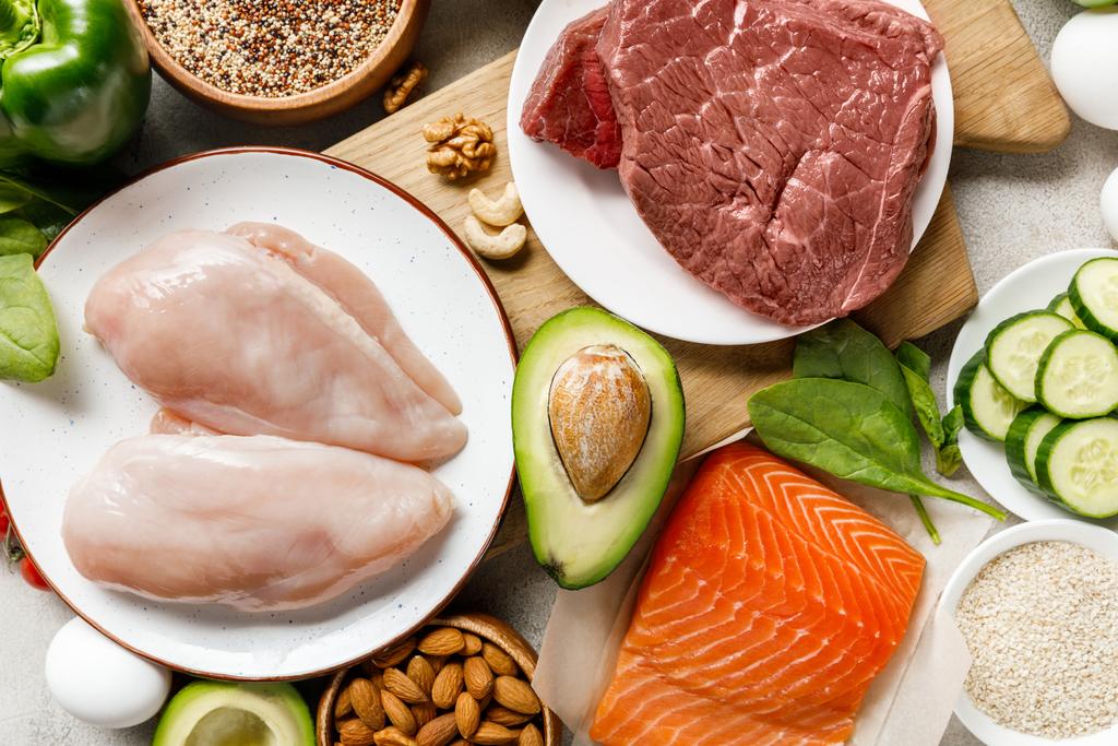 top view of fresh raw salmon, meat and chicken breasts near nuts and vegetables, ketogenic diet menu - Photo, Image