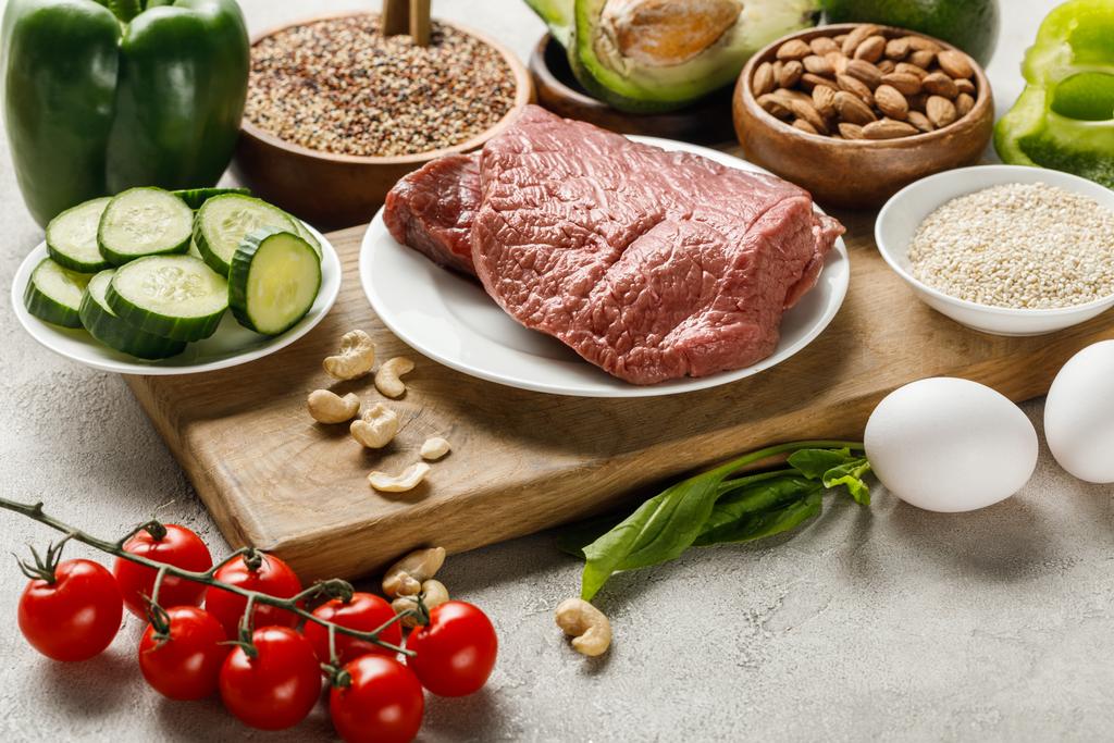 carne fresca cruda sobre tabla de cortar de madera cerca de nueces, verduras y grañones, menú de dieta cetogénica
 - Foto, imagen