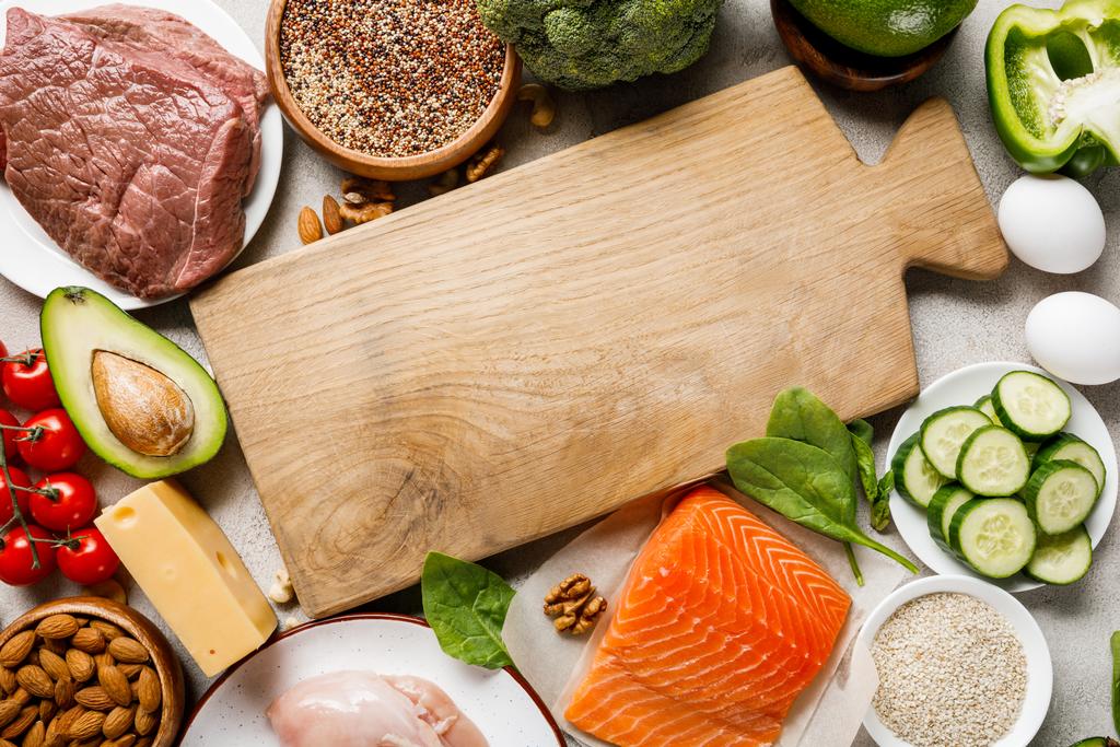 top view of raw salmon, chicken breasts and meat near nuts, dairy products and vegetables around wooden chopping board with copy space, ketogenic diet menu - Photo, Image