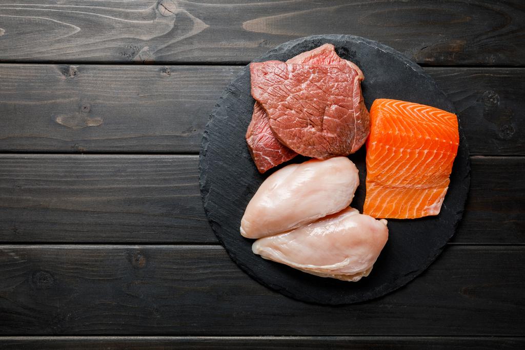 Κορυφαία όψη του φρέσκου ακατέργαστου σολομού, κρέας και στήθος κοτόπουλου στο ξύλινο μαύρο τραπέζι, το μενού της κετονέας δίαιτας - Φωτογραφία, εικόνα