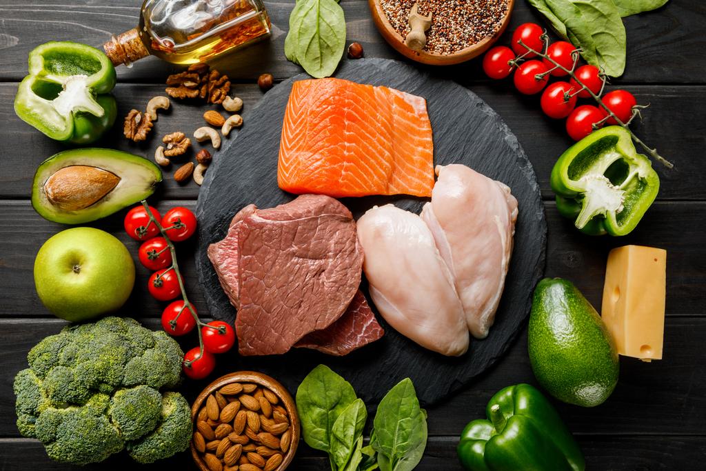 Widok z góry surowego łososia, mięsa i piersi z kurczaka na drewnianym czarnym stole z warzywami i nakrętkami, menu dietetyczne ketogeniczne - Zdjęcie, obraz