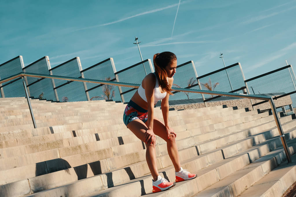 Lunghezza piena di bella giovane donna in abbigliamento sportivo rilassante durante l'esercizio all'aperto, in piedi su scale con recinzione
  - Foto, immagini