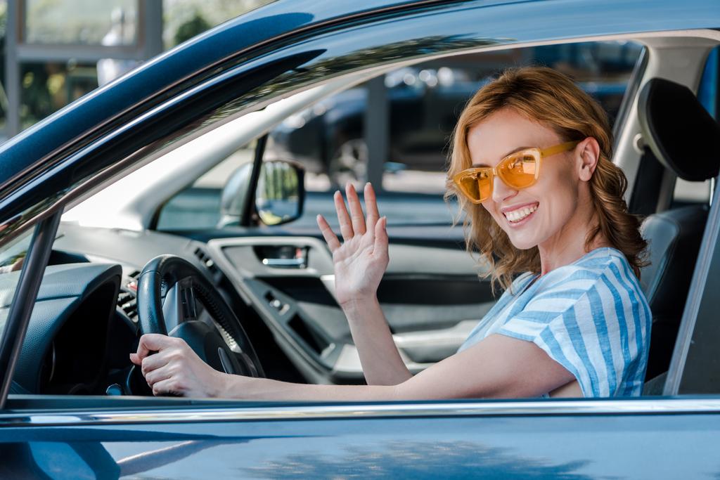 femme gaie dans les lunettes de soleil agitant la main tout en conduisant voiture
  - Photo, image
