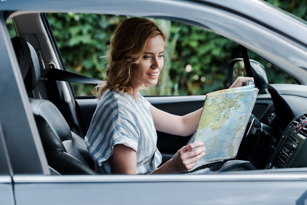 Selektywna koncentracja atrakcyjna kobieta patrząc na mapie i jazdy samochodem  - Zdjęcie, obraz