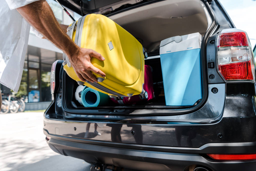 cropped view of man putting yellow luggage in car trunk  - Photo, Image