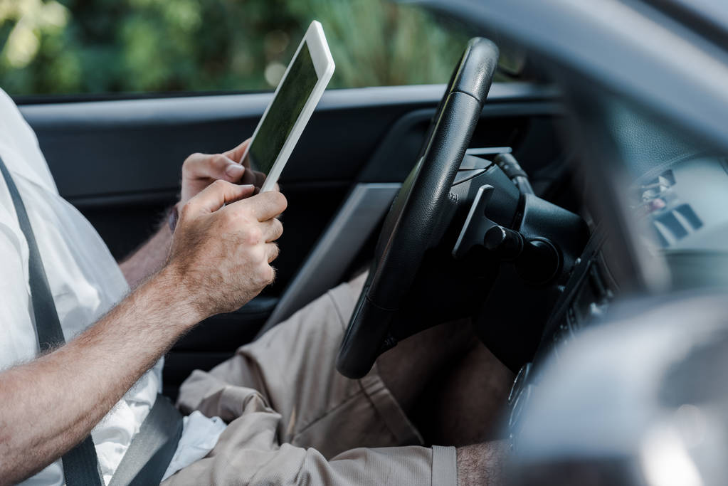 περικομμένη όψη του ανθρώπου που κάθεται στο αυτοκίνητο και κρατώντας το ψηφιακό δισκίο  - Φωτογραφία, εικόνα