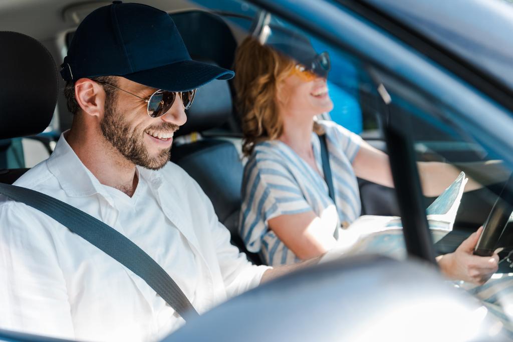 επιλεκτική εστίαση του ευτυχισμένο άνθρωπο σε γυαλιά ηλίου χαμογελώντας με τη γυναίκα στο αυτοκίνητο  - Φωτογραφία, εικόνα