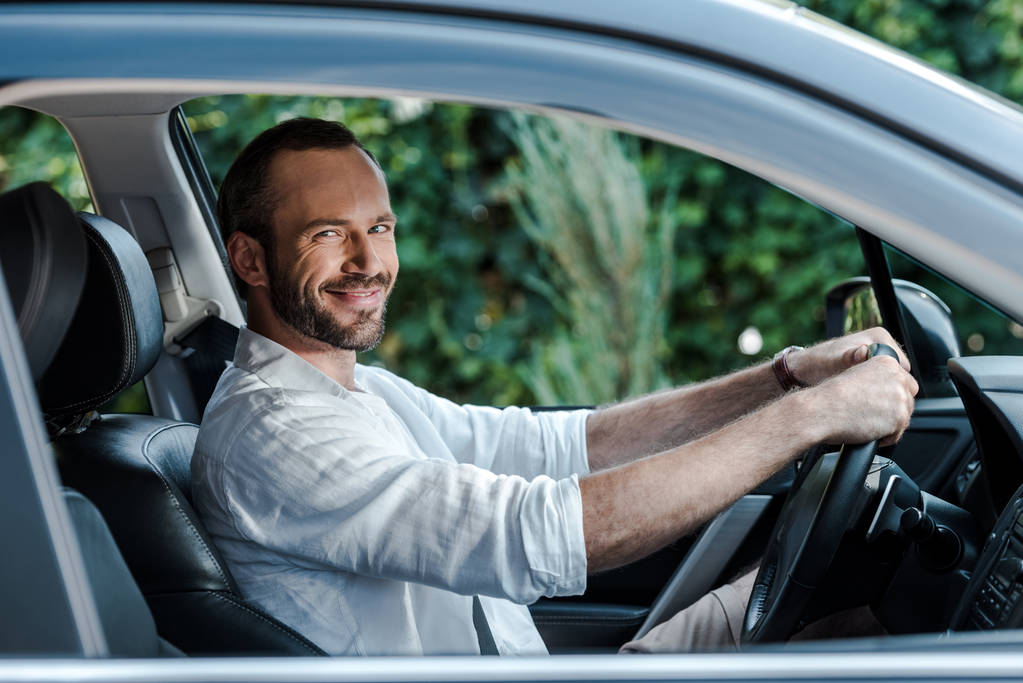 車を運転しながら笑顔とカメラを見て幸せなあごひげの男の選択的な焦点  - 写真・画像