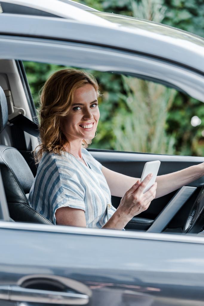 enfoque selectivo de la mujer feliz sosteniendo teléfono inteligente en el coche
  - Foto, imagen