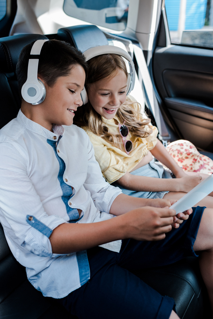szelektív középpontjában vidám gyerekek hallgat zenét fejhallgató nézésekor okostelefon az autóban  - Fotó, kép