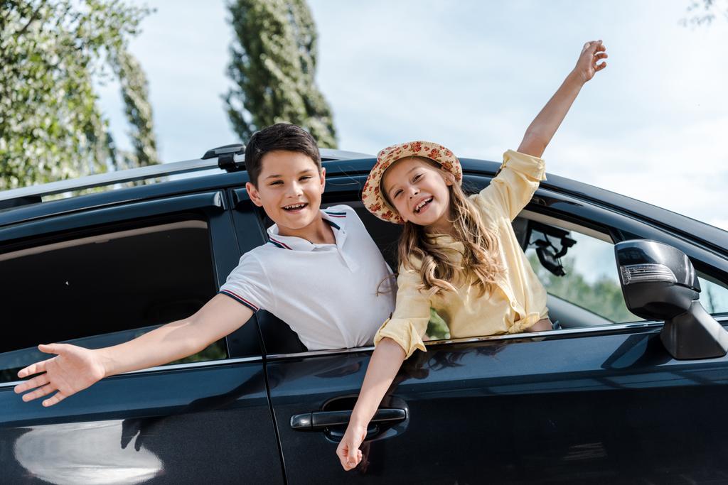 niski kąt widzenia szczęśliwych dzieci z wyciągniętymi rękami w oknach samochodowych  - Zdjęcie, obraz