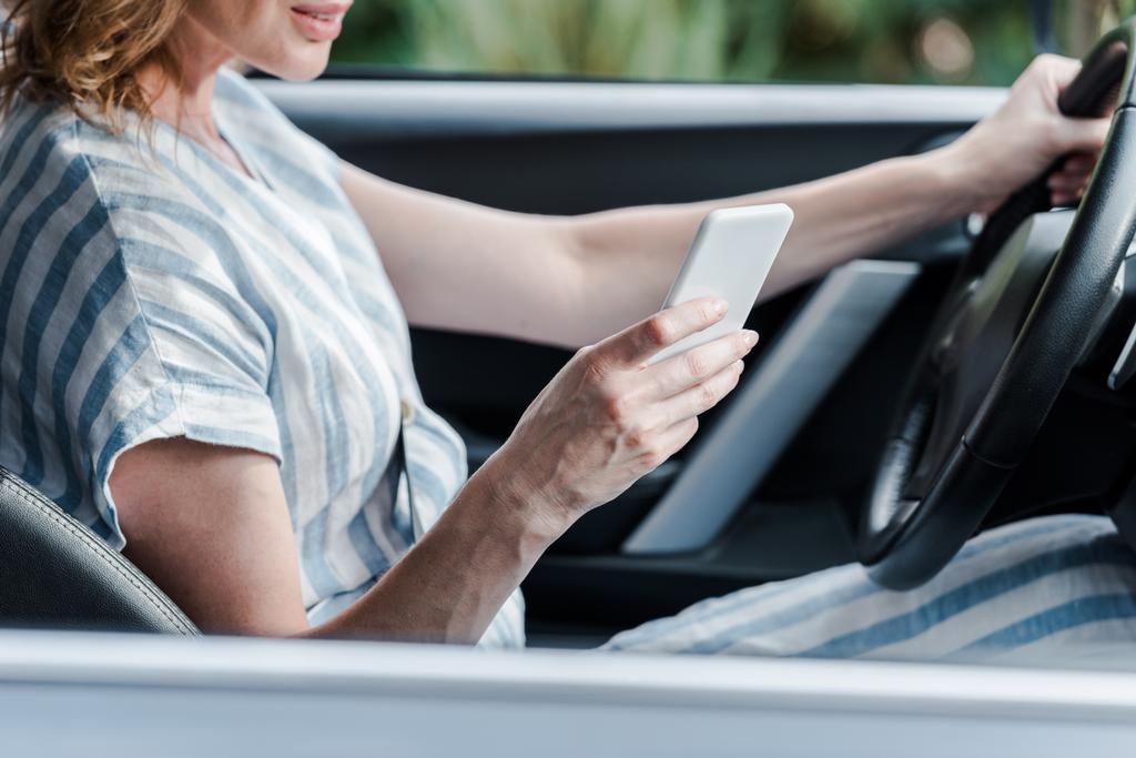 visão recortada da mulher segurando o volante e usando o smartphone no carro
  - Foto, Imagem