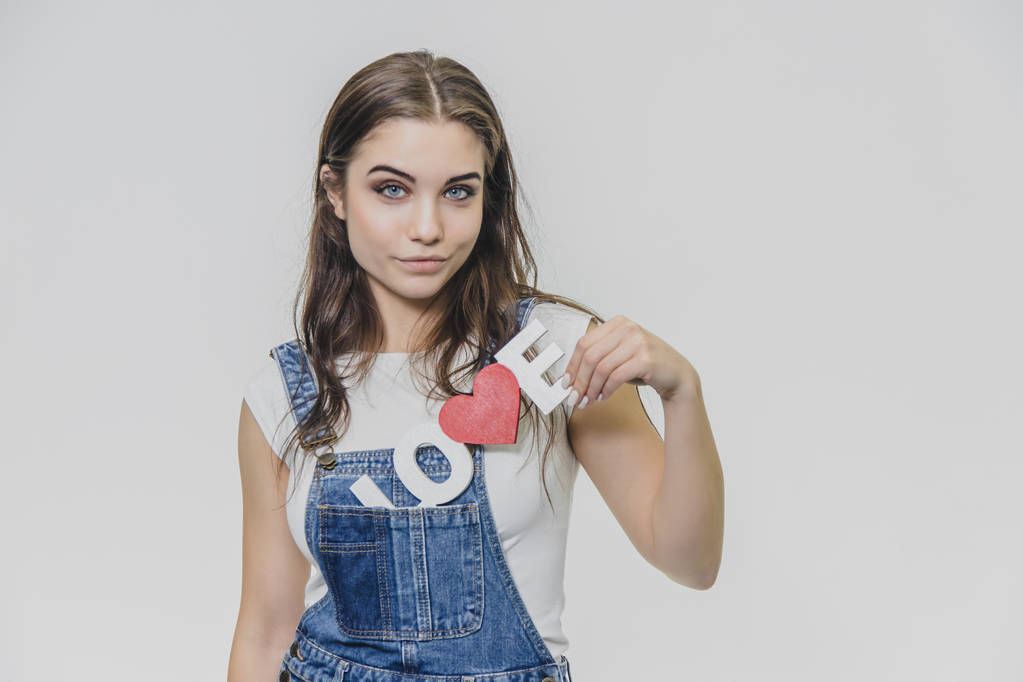 Horizontal portrait of a beautiful woman with a puzled expression, finds a solution, wearing a casual denim overalls. Isolated on a gray background. - Photo, Image