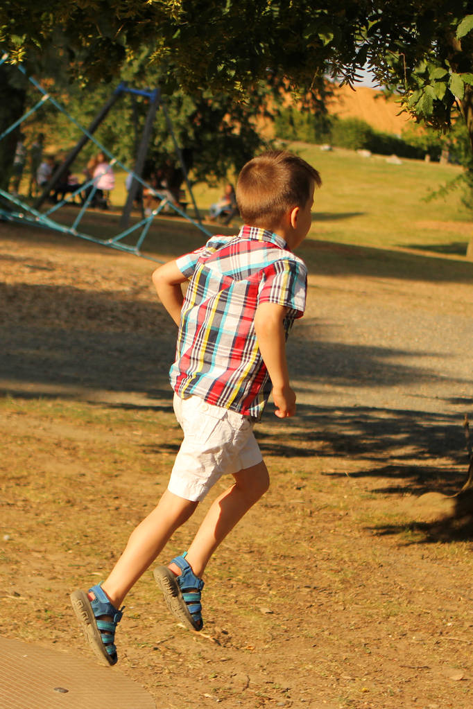 Junge im karierten Hemd springt und rennt im Park, das Konzept einer glücklichen Kindheit - Foto, Bild