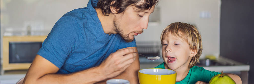 Padre e hijo están hablando y sonriendo mientras desayunan en la cocina BANNER, LARGO FORMATO
 - Foto, imagen
