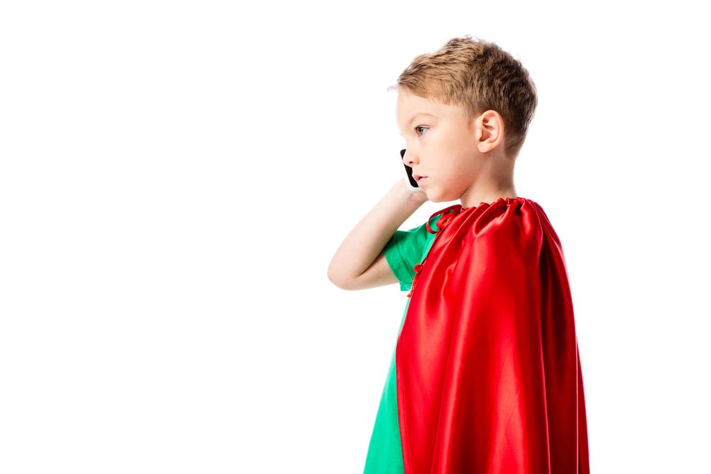 visão lateral do menino pré-escolar sério em capa de herói vermelho falando no smartphone isolado no branco
 - Foto, Imagem