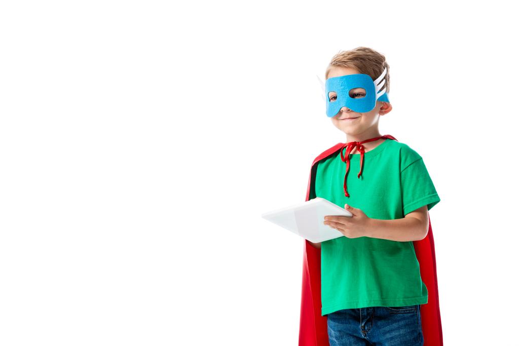 usmívající se dítě v masce a v plášti červeného hrdiny, s použitím digitálního tabletu izolovaného na bílém - Fotografie, Obrázek