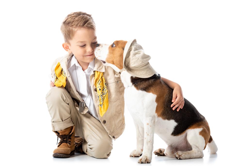 χαμογελαστή νήπιο εξερευνητής παιδί αγκαλιάζοντας σκυλί κυνηγόσκυλο στο καπέλο σε λευκό - Φωτογραφία, εικόνα