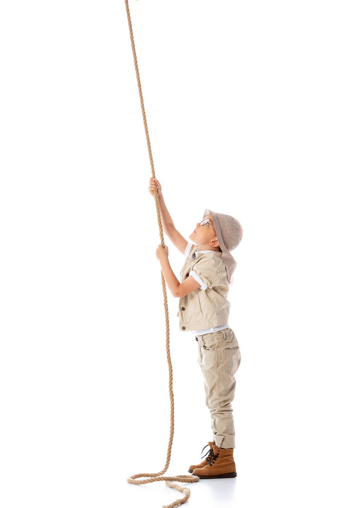 白に隔離されたロープを保持する帽子と眼鏡で焦点を当てた探検家の子供の完全な長さのビュー - 写真・画像