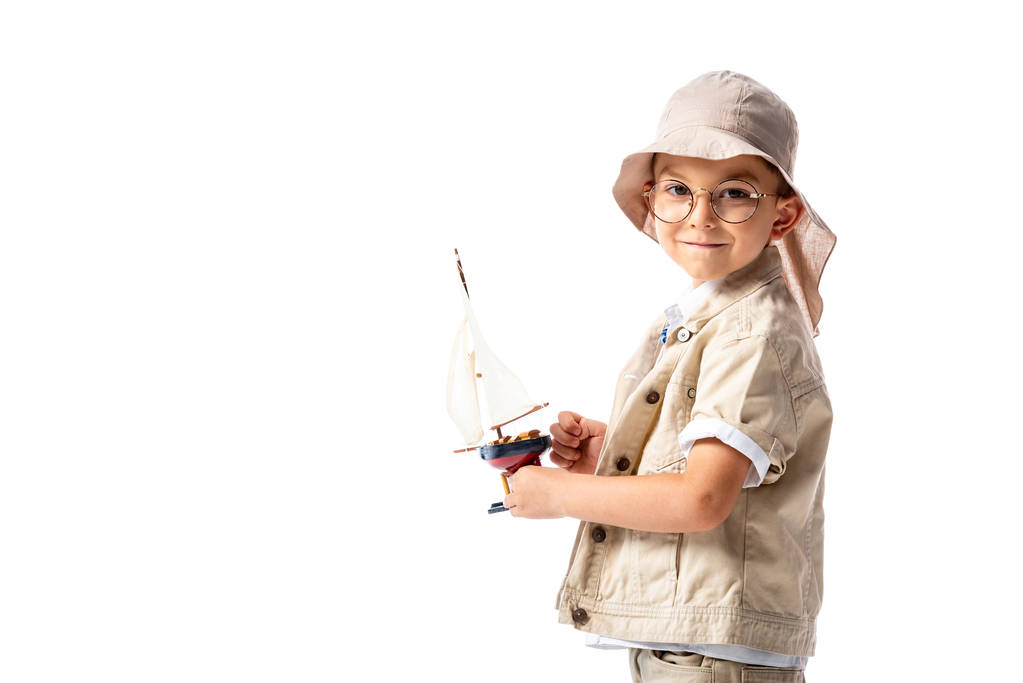 χαμογελαστός εξερευνητής παιδί σε ποτήρια και καπέλο κράτημα παιχνίδι πλοίο απομονωμένη σε λευκό - Φωτογραφία, εικόνα