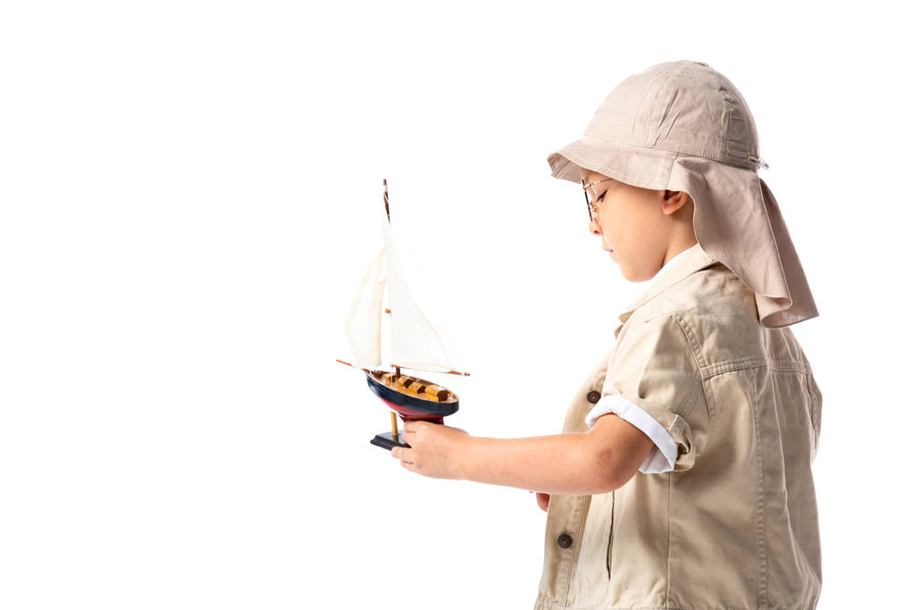 side view of explorer child in glasses and hat holding toy ship isolated on white - Photo, Image