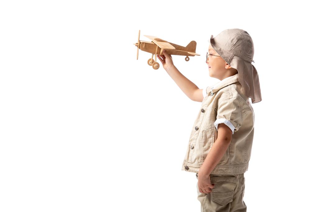 vue latérale du garçon explorateur souriant dans des lunettes et un chapeau tenant l'avion jouet en bois isolé sur blanc
 - Photo, image