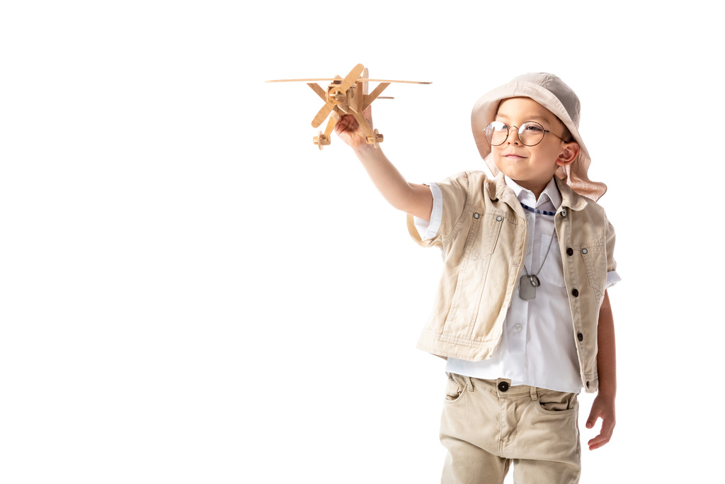 白で隔離された木製のおもちゃの飛行機を保持する眼鏡と帽子で笑顔の探検家の少年 - 写真・画像