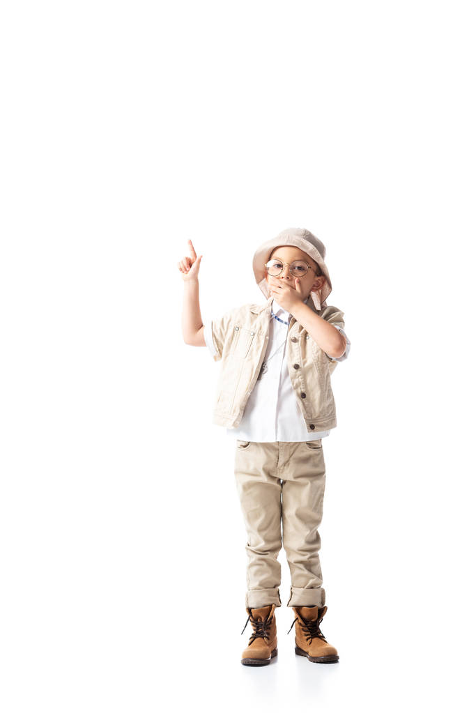 pełny widok długości zszokowany chłopiec Explorer w kapeluszu i okulary pokazując znak pomysł i obejmujące usta z ręki na białym - Zdjęcie, obraz