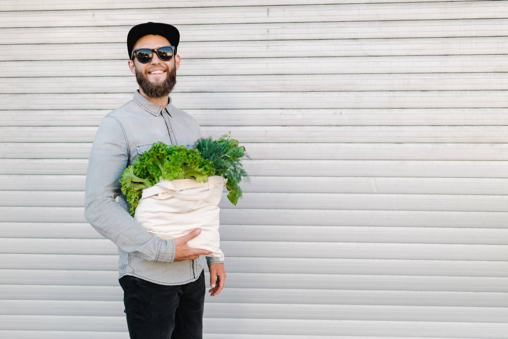 Muž, který drží ekotašku naplněnou potravinami. Z vaku visí zelenina a ovoce. Ekologie koncepce ochrany životního prostředí - Fotografie, Obrázek