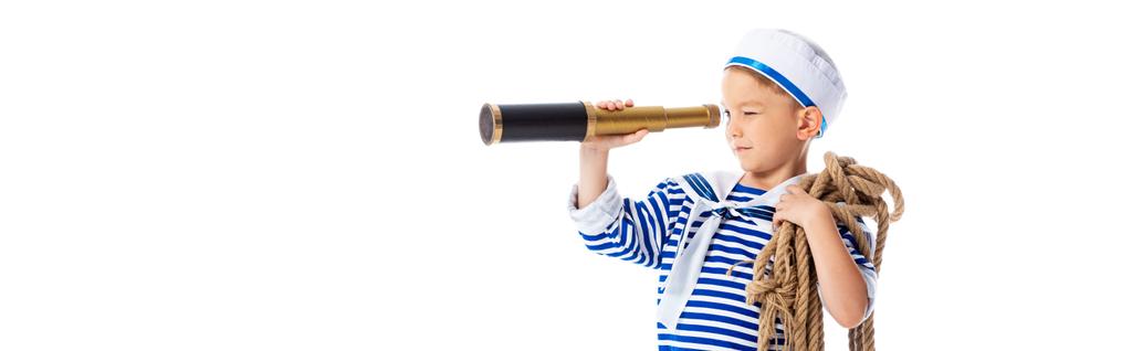 panoramic shot of focused boy in sailor costume holding rope and looking through spyglass isolated on white - Photo, Image