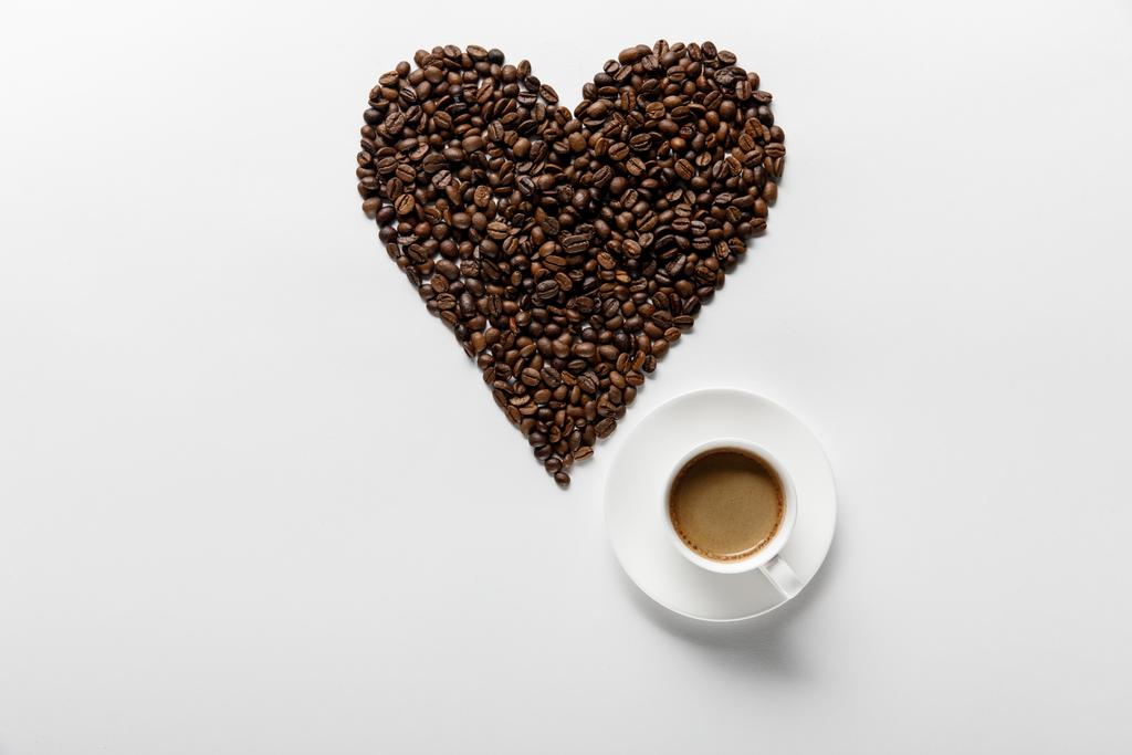 beyaz arka plan üzerinde kahve taneleri yapılmış kalp ile kahve üst görünümü - Fotoğraf, Görsel