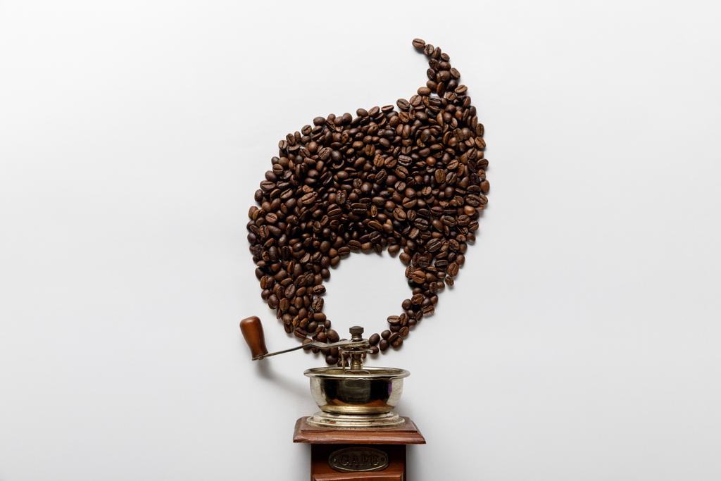 白い背景にコーヒー粒で作られた炎の近くのヴィンテージコーヒーグラインダーのトップビュー - 写真・画像