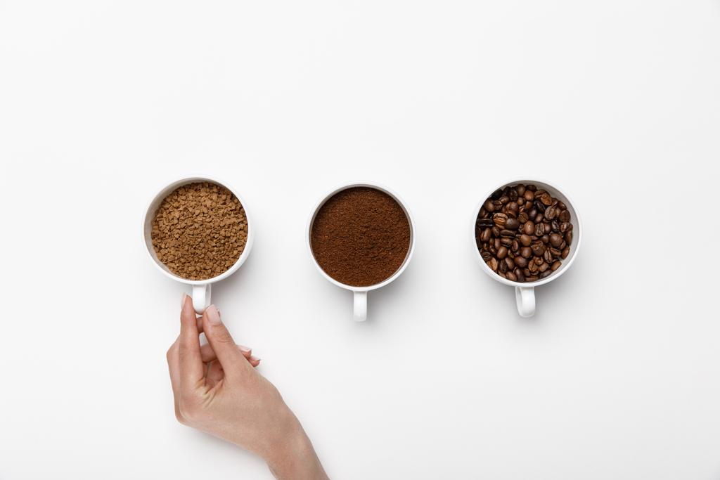 vista recortada de la mano femenina cerca de tres tipos de molienda de café en tazas sobre fondo blanco
 - Foto, imagen