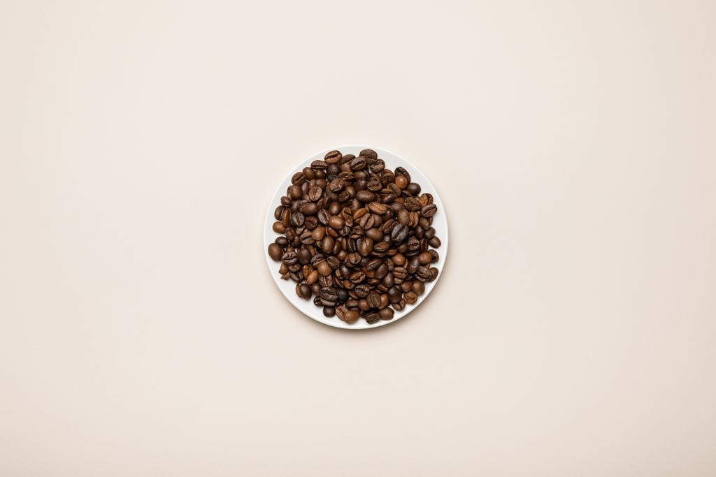 вид зверху на кавові зерна на білій тарілці на бежевому фоні
 - Фото, зображення
