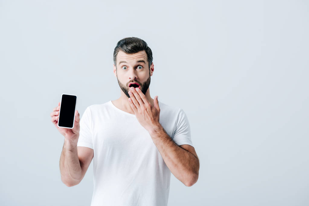 hombre sorprendido cubriendo la boca y mostrando teléfono inteligente con pantalla en blanco aislado en gris
 - Foto, Imagen