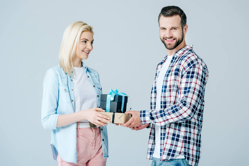 усміхнений чоловік дарує подарунки красивій дівчині ізольовані на сірому
 - Фото, зображення
