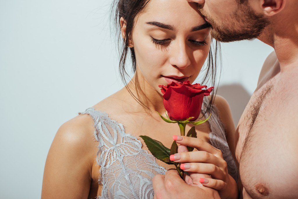 przystojny nagi człowiek Całowanie sympatia w czoło podczas dziewczyna wąchania czerwony Róża - Zdjęcie, obraz