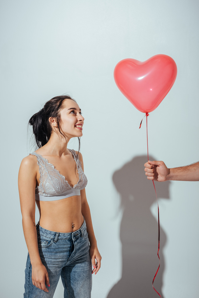 περικομμένη θέα του ανθρώπου δίνοντας κόκκινο μπαλόνι σε μορφή καρδιάς σε ελκυστικό κορίτσι - Φωτογραφία, εικόνα