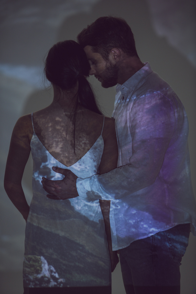 junger Mann umarmt Freundin, während er in der Dunkelheit steht - Foto, Bild
