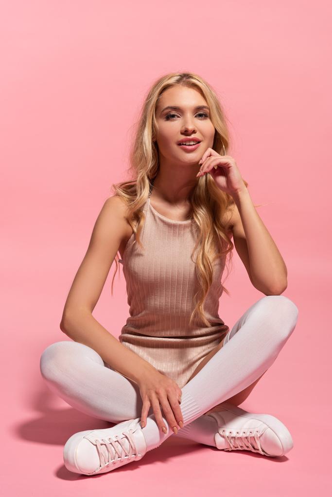 krásná blondýnka v kamaše, která sedí s zkřížené nohy na růžovém - Fotografie, Obrázek