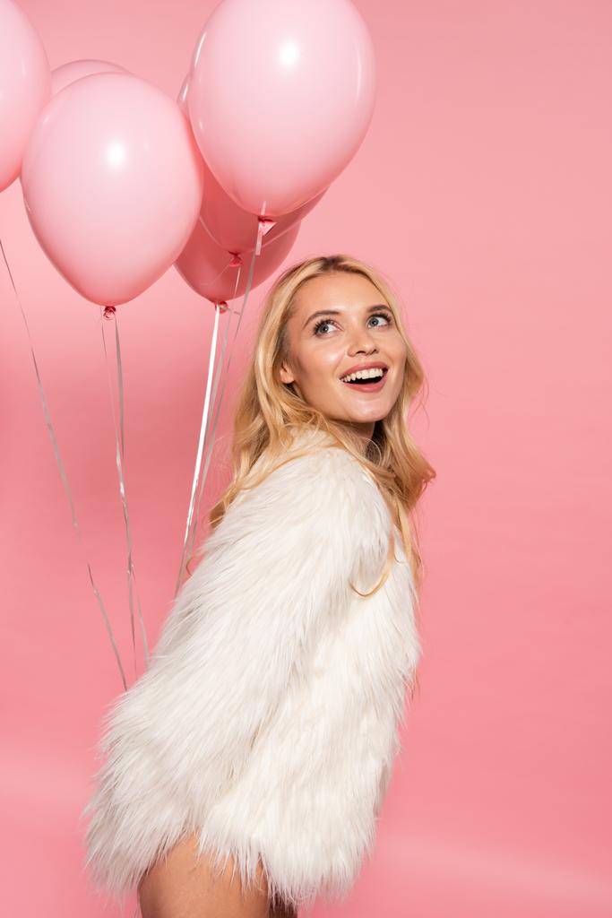 счастливая красивая сексуальная блондинка в белой шубе с воздушными шариками на розовом фоне
 - Фото, изображение