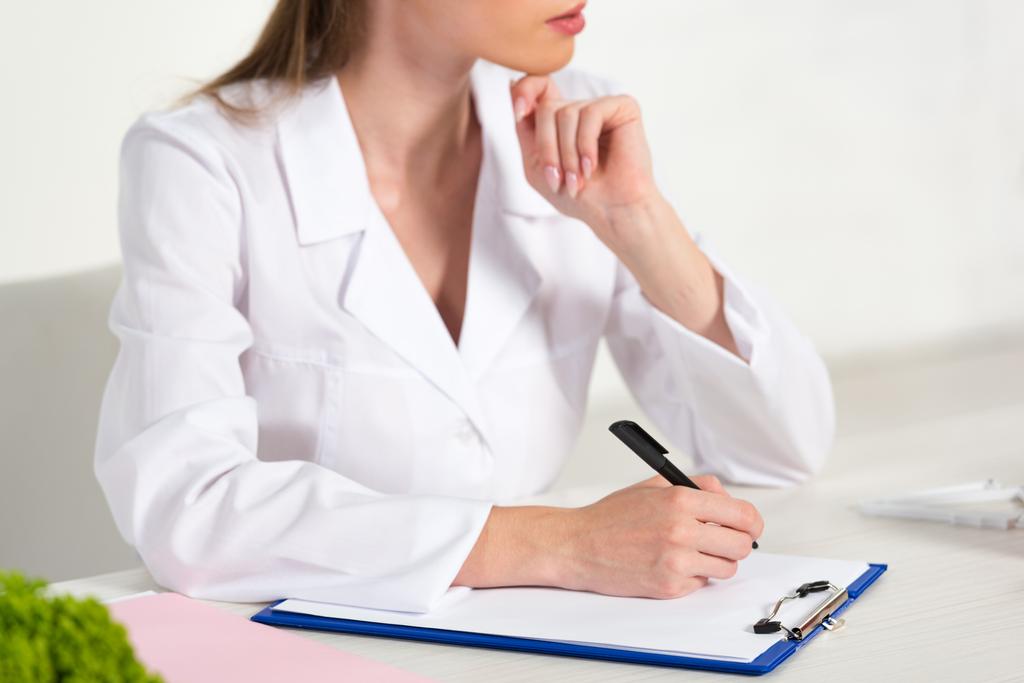 osittainen näkemys ravitsemusterapeutin valkoisessa takissa kirjallisesti leikepöydällä työpaikalla
 - Valokuva, kuva